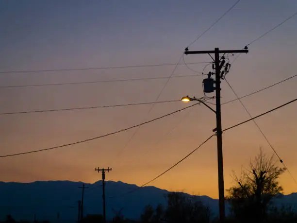 Silhouette of electricity poles and streetlamp at lonely desert road cross during twilight