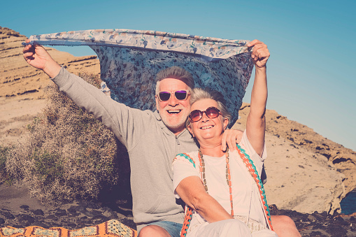 retired and vacation freedom concept for hippy senior couple man and woman playing with the wind with colored clothes. pastel tones and blue sky for smiling people