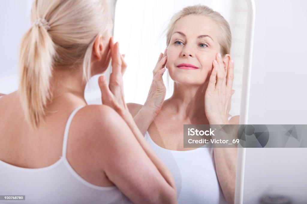 Femme regardant les rides en miroir d’âge moyen. Chirurgie plastique et injections de collagène. Maquillage. Visage de macro. Mise au point sélective - Photo de Produit anti-âge libre de droits