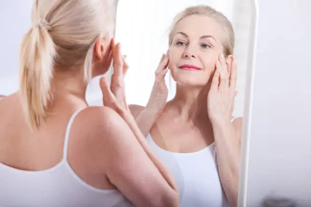 Photo of Middle aged woman looking at wrinkles in mirror. Plastic surgery and collagen injections. Makeup. Macro face. Selective focus