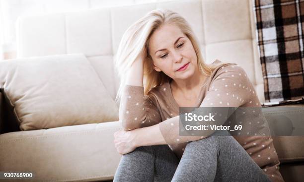 Middle Aged Barefoot Woman Sitting At The Floor Embracing Her Knees Near Sofa At Home Her Head Down Bored Troubled With Domestic Violence Stock Photo - Download Image Now