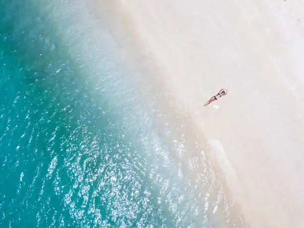 Woman sunbathing on the white sand beach. Aerial straight drone shot. Lombok island