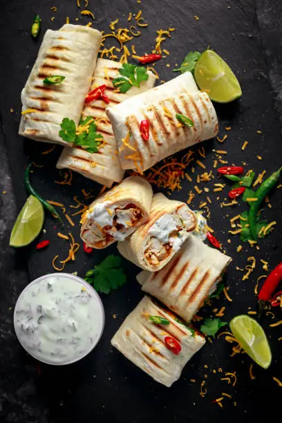 Healthy grilled chicken and parsley wraps, loaded with cheese, served with greek yogurt deep, chillies and lime slices.