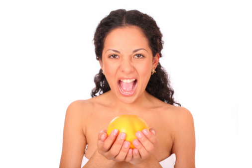 A woman holds an orange in her hands, standing on white background.