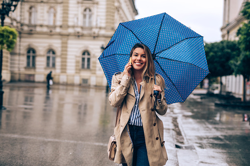 Young woman talking on the mobile phone while holding an umbrella outdoors.