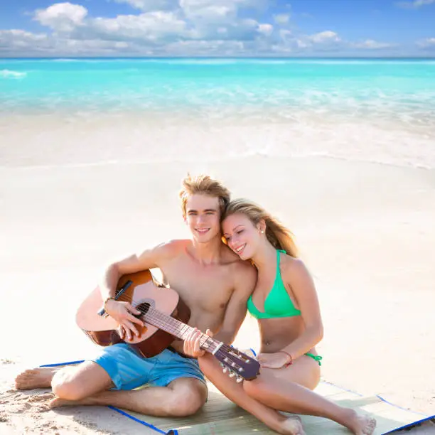 Blond young tourist couple playing guitar at beach