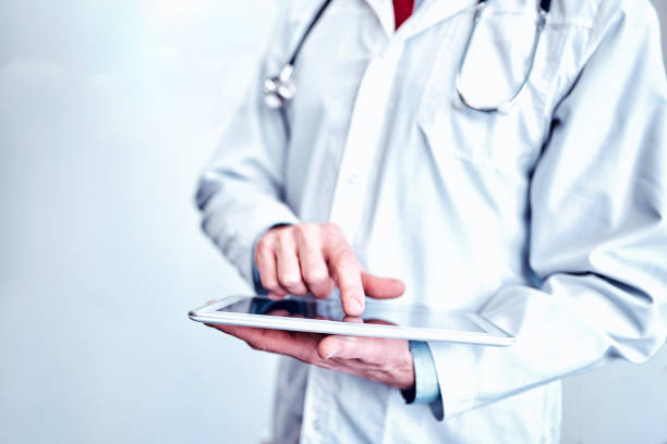 doctor in white medical coat  is using a tablet and smiling while standing against window stock photo
