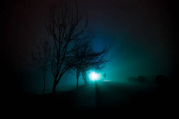 Night Landscape. City at night in dense fog. Mystical landscape surreal lights with creepy man. The walking man's silhouette in night fog at artificial light. Beautiful mixed lighting from backside.
