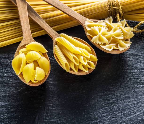 istock Different pasta types in wooden spoons on the table. 930864074