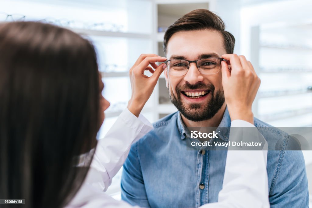 Doctor and patient in ophthalmology clinic Young female doctor ophthalmologist is helping handsome man to choose the most appropriate eyeglasses. Doctor and patient in modern ophthalmology clinic Optometrist Stock Photo