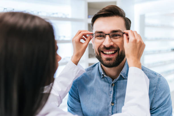 Doctor and patient in ophthalmology clinic Young female doctor ophthalmologist is helping handsome man to choose the most appropriate eyeglasses. Doctor and patient in modern ophthalmology clinic optometry photos stock pictures, royalty-free photos & images