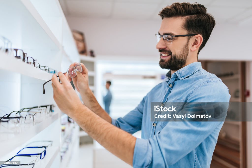 Patient in ophthalmology clinic Handsome young man is choosing the most appropriate eyeglasses in modern ophthalmology clinic. Optometrist Stock Photo