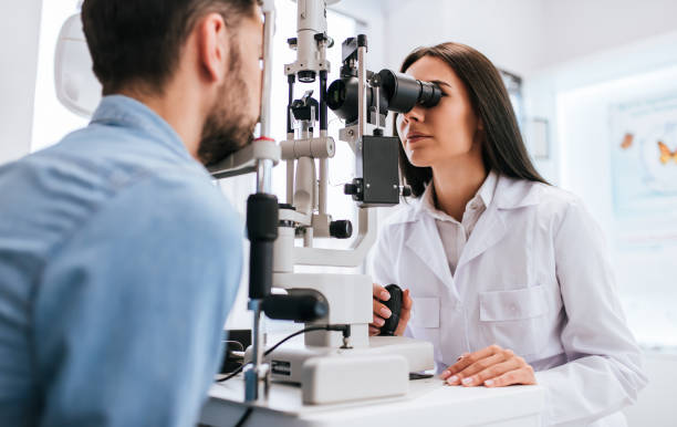 Doctor and patient in ophthalmology clinic Attractive female doctor  ophthalmologist is checking the eye vision of handsome young man in modern clinic. Doctor and patient in ophthalmology clinic. optical equipment stock pictures, royalty-free photos & images