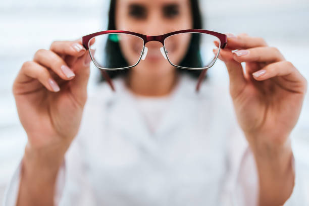 Female doctor in ophthalmology clinic Cropped image of attractive young female doctor in ophthalmology clinic. Doctor ophthalmologist is standing near shelves with different eyeglasses. lens optical instrument stock pictures, royalty-free photos & images