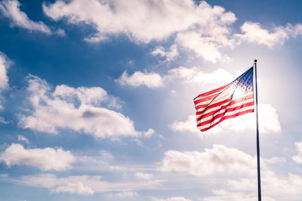 istock Blue Sky, Puffy Clouds, and American Flag waving into the Sunshine 930881918