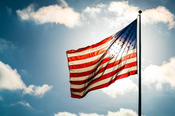 blauer himmel, geschwollenen wolken und amerikanische flagge winken in den sonnenschein hautnah - flag american culture flying sky stock-fotos und bilder