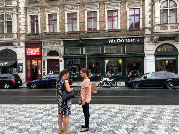 due ragazze in piedi, che visitano per strada visitando dall'altra parte della strada da un fast food mcdonaldâs sulla strada principale di praga. - cicada foto e immagini stock