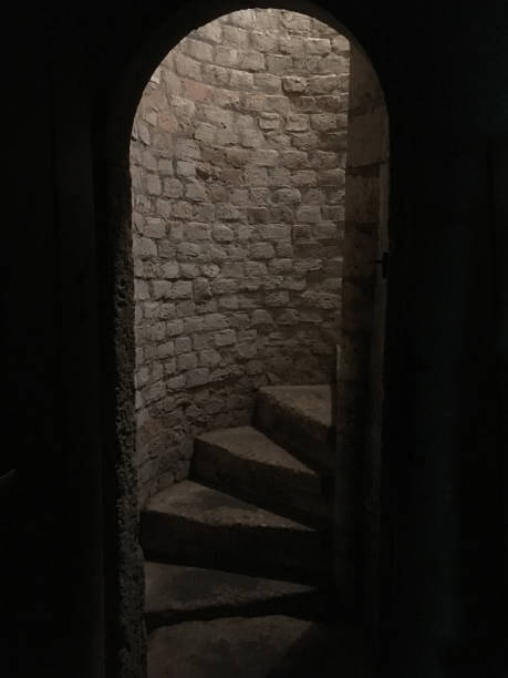 istock Medieval stone spiral staircase, steps going up to ground floor. Medieval dungeon. Stone steps framed by arched doorway. Going down the basement of a castle. 930889870