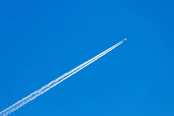 Modern jet plane with white condensation track flies on a blue sky background Modern jet plane with white condensation track flies on a blue sky background all weather running track stock pictures, royalty-free photos & images