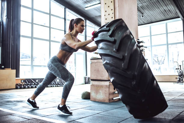 Sporty woman in gym Attractive young sporty woman is working out in gym. gym training. Pushing big tire. woman pushing tire stock pictures, royalty-free photos & images