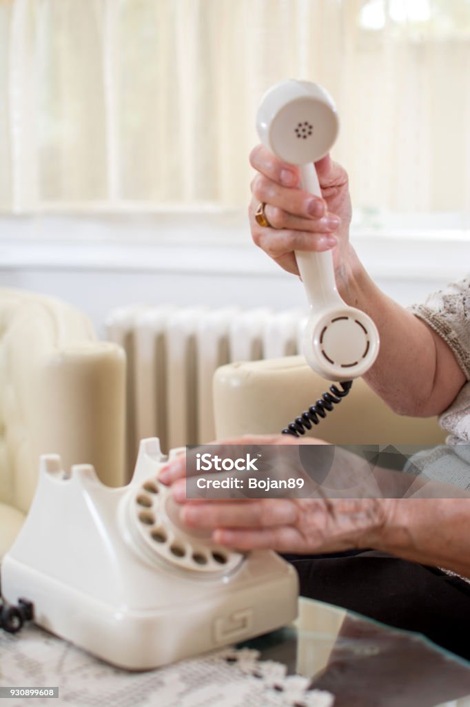 Close up of wrinkled senior's hands dialing phone number on rotary telephone in old-fashioned ambient. Telephone Stock Photo