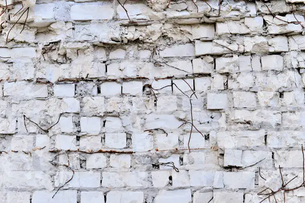 Photo of Part of the wall of white brick with pieces of rebar of an old building for demolition.