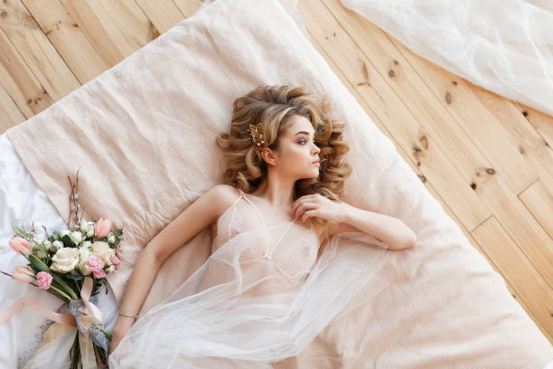 belle jeune mariée en lingerie sexy se trouve sur un lit avec un bouquet de fleurs. vue horizontale supérieure - sensuality sex symbol dressing room women photos et images de collection