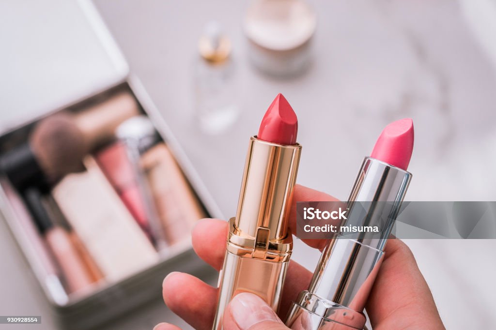 Set of decorative cosmetic. A person holds two lipsticks. Beauty products blurred background. Top view. Lipstick Stock Photo