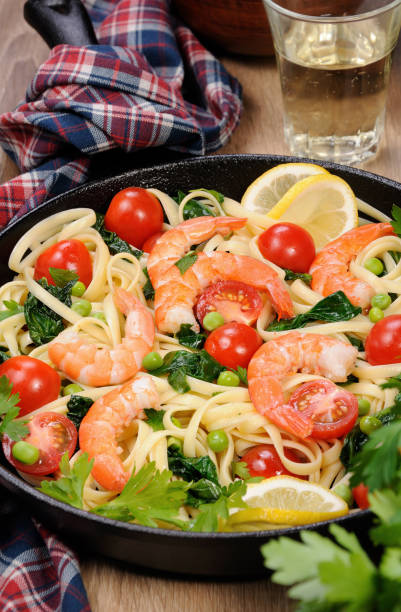 pâtes aux crevettes frits, petits pois, tomates et épinards dans une poêle, sur une table avec des verres de cidre. - carbohydrate diabetes pasta food photos et images de collection