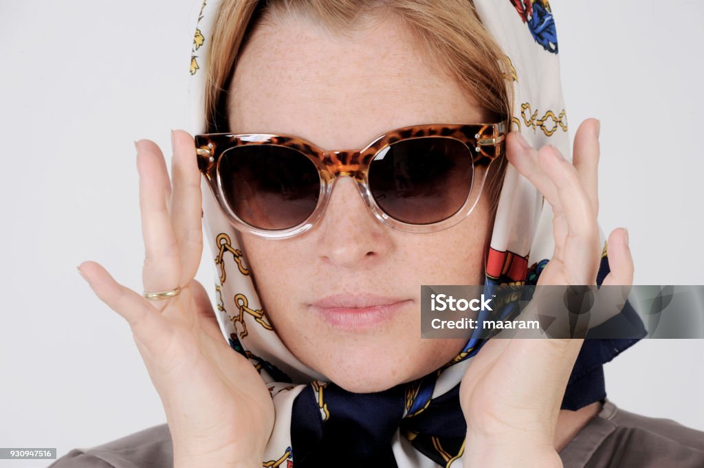 Young woman is wearing scarf and sunglasses in a Grace Kelly Style. Young woman is wearing scarf and sunglasses in a Grace Kelly Style. Studio shot with light background. Isolated. Human Face Stock Photo