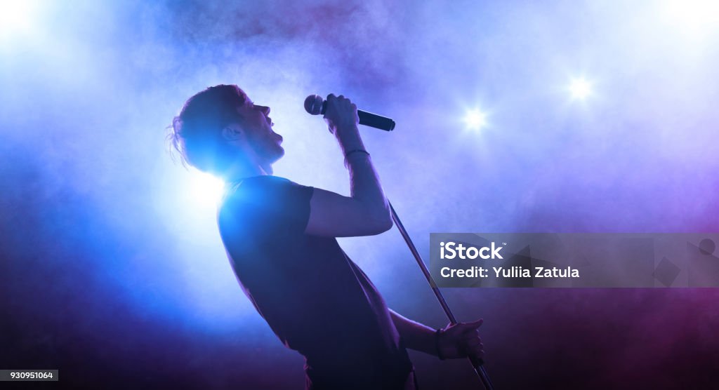 Singer with a microphone performing on stage Young vocalist with a microphone singing on stage Singing Stock Photo