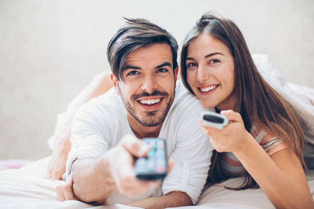 istock Couple with two tv remote controls lying in bed 931004134