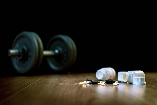 steroid pills and capsules with dumbbell weight in the background - doping in sport. - doping imagens e fotografias de stock