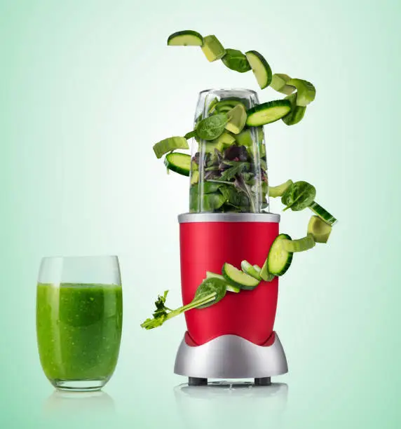 Smoothie maker mixer with vegetable flying ingredients, isolated on green background. Healthy drink and lifestyle