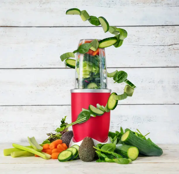 Smoothie maker mixer with vegetable flying ingredients, placed on wooden background. Healthy drink and lifestyle