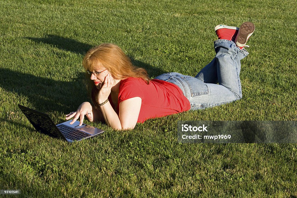 Red headed woman using laptop lying on the grass  40-44 Years Stock Photo