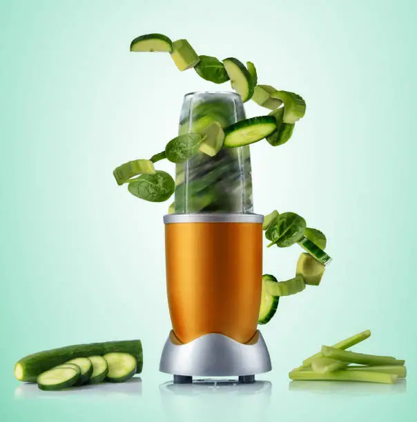 Smoothie maker mixer with vegetable flying ingredients, isolated on green background. Healthy drink and lifestyle