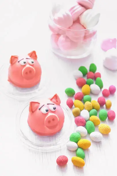 Sweet delicate macaroons of pink marzipan in the form of a mini-pig marshmallows, peanuts in sugar pastel colours on a light background with place for text. Close up.
