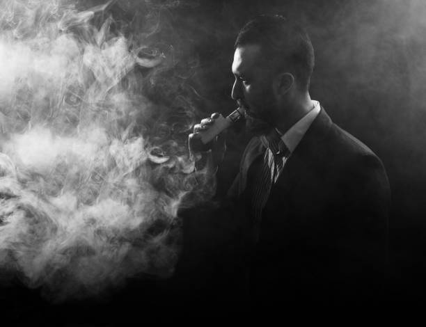 istock Vaping man holding a mod. A cloud of vapor. Black background. 931051330