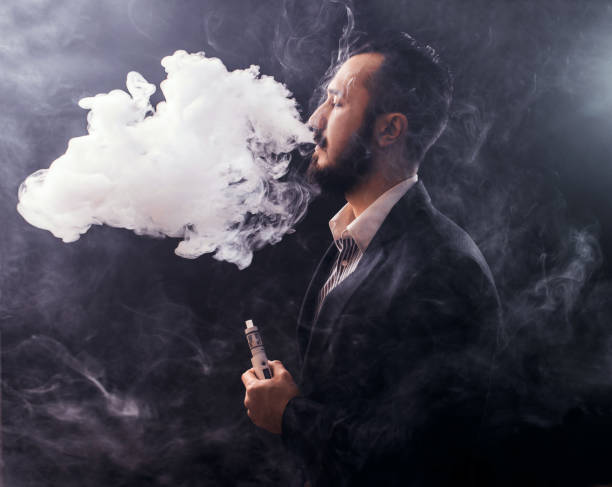 istock vaping man holding a mod. A cloud of vapor. Black background. 931051340
