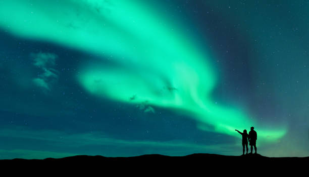 Aurora borealis and silhouette of man and woman Aurora borealis and silhouette of standing man and woman who pointing finger on northern lights. Lofoten islands,Norway. Aurora. Sky with stars and polar lights. Night landscape with aurora and couple star sky night island stock pictures, royalty-free photos & images