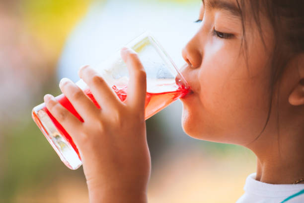 Cute asian little child girl drinking red juice water with ice from glass stock photo