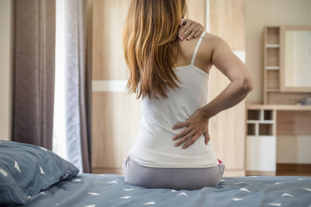 woman suffering from back ache on the bed - dor de costas imagens e fotografias de stock