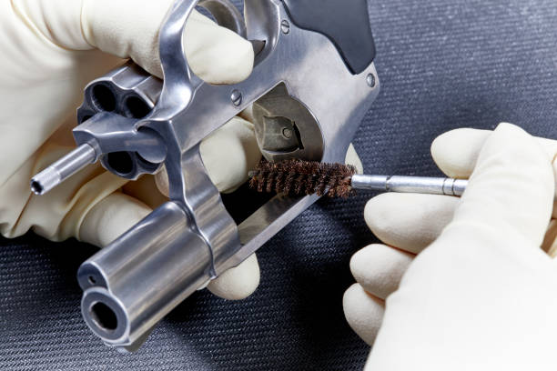 Man`s hand cleaning the gun rifle parts details by special metal cleaning rod red plastic holder background top view