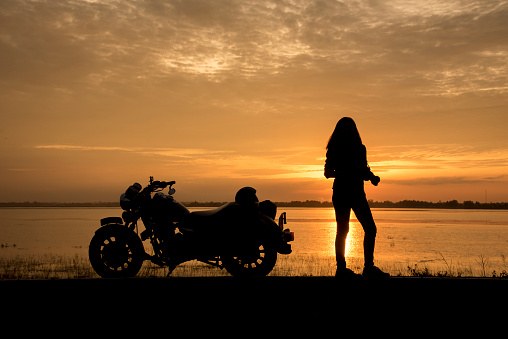 Beautiful Woman biker enjoying sunset, female riding motorcycle. motorbike driver traveling the world, Relaxing after long trip, freedom lifestyle. Travel Concepts.