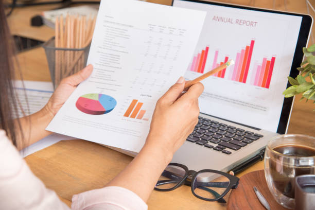 istock Top view of young working woman using laptop and reading annual report document at work. Business woman working at her desk. 931087416