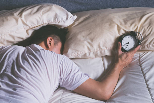 sleeping asian young male disturbed by alarm clock early morning in bed stock photo
