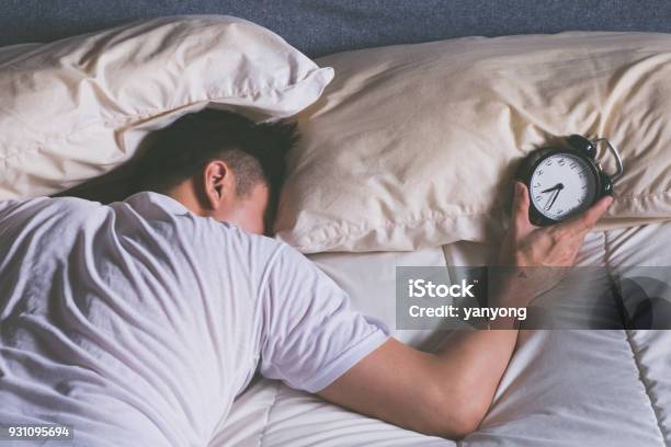 Sleeping Asian Young Male Disturbed By Alarm Clock Early Morning In Bed Stock Photo - Download Image Now