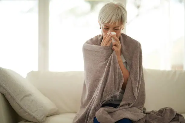 Shot of a senior woman blowing her nose with a tissue at home