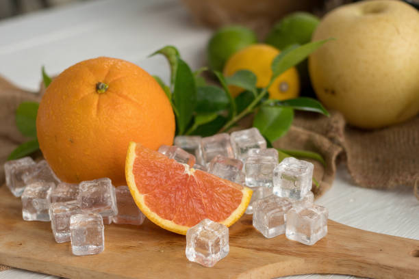 Orange and sliced on a wooden plate with ice cubes and fruit as background.